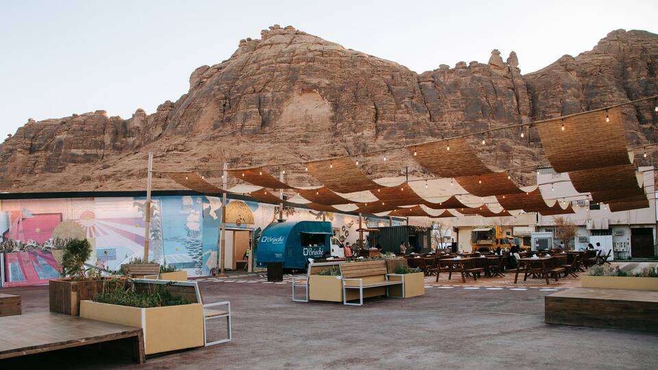 An outdoor seating area with a mountain backdrop, a food truck, and a mural.
