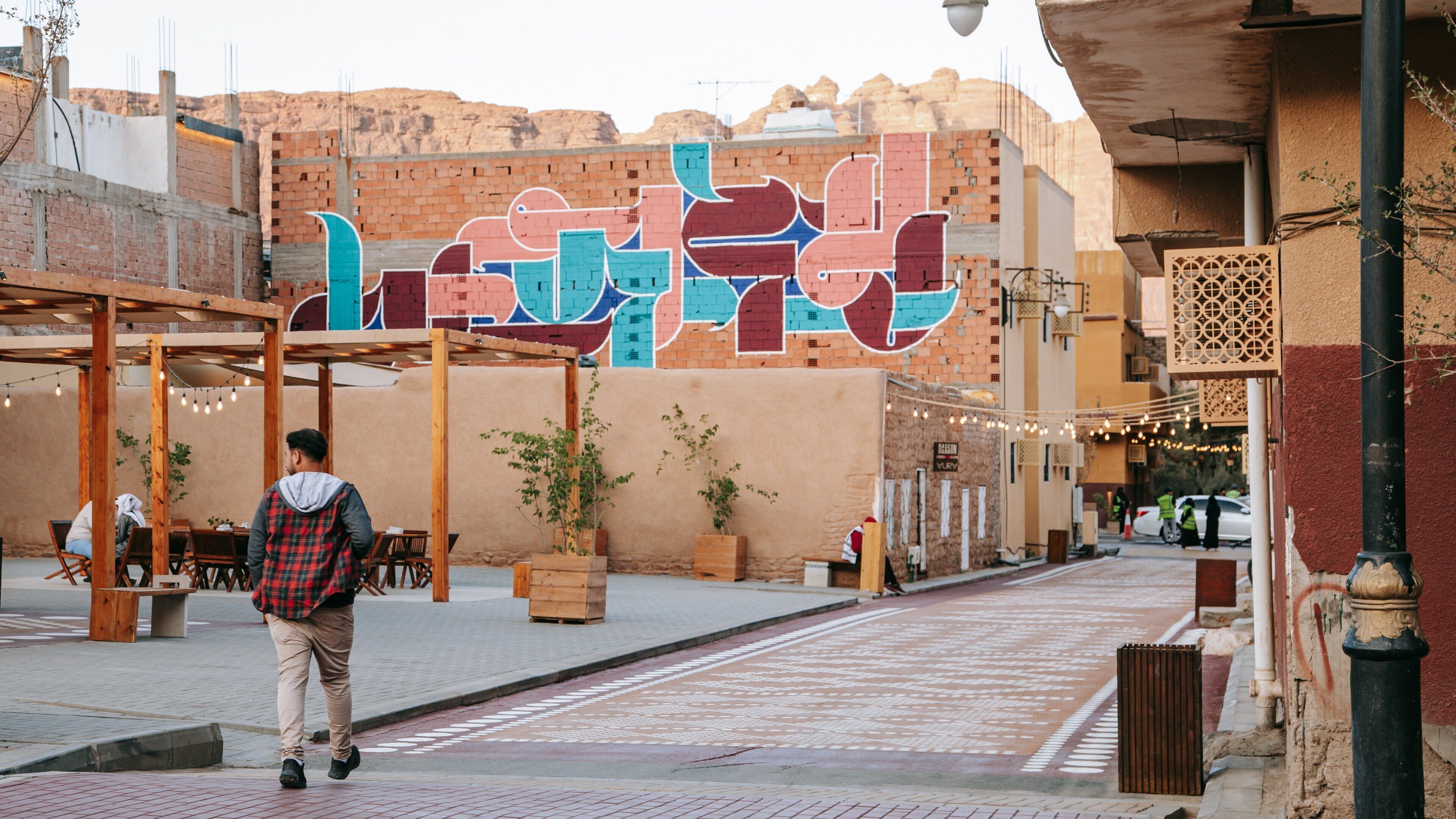A man walking on a paved street with a colorful mural in the background.