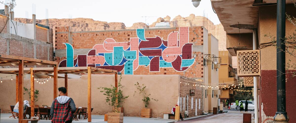 A man walking on a paved street with a colorful mural in the background.