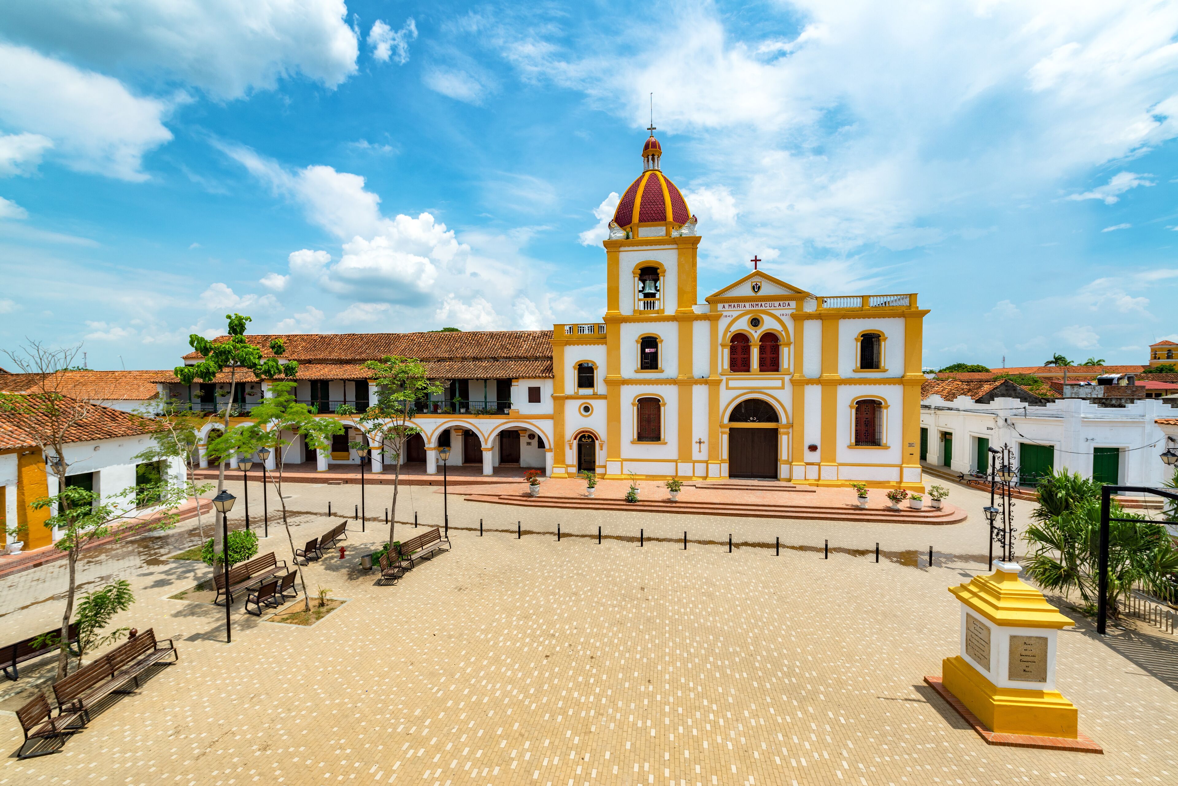 A colonial-style church with a prominent bell tower and a paved plaza with benches.