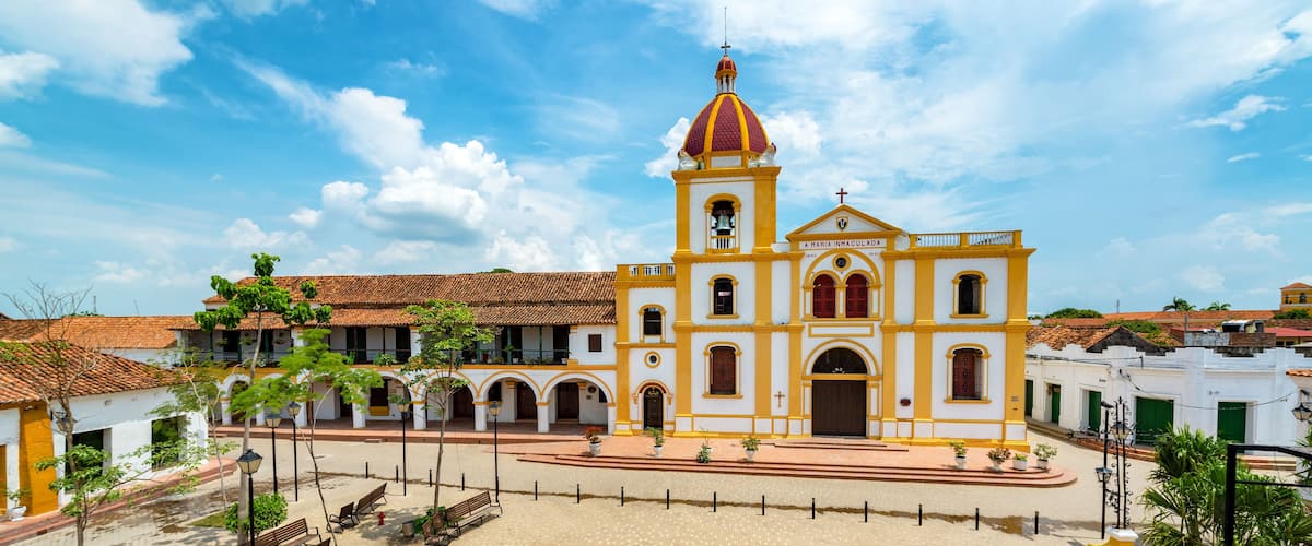 A colonial-style church with a prominent bell tower and a paved plaza with benches.