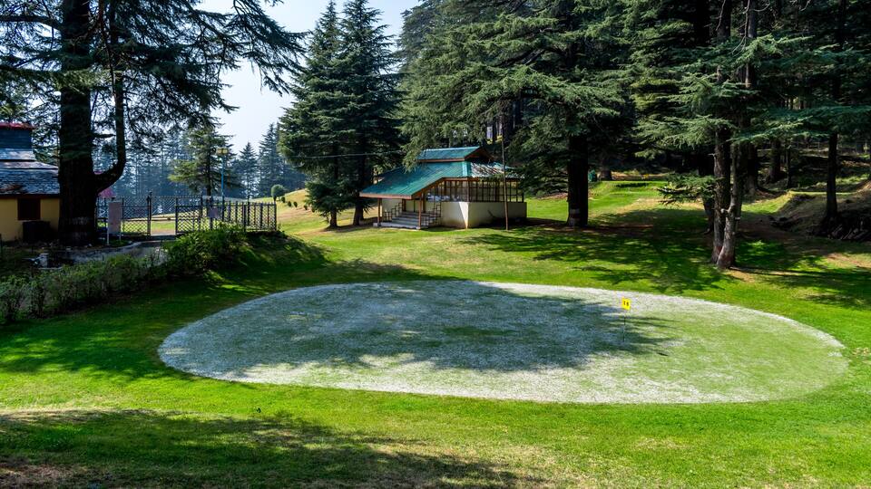 A golf course with a tee box, a putting green, and a clubhouse surrounded by trees.