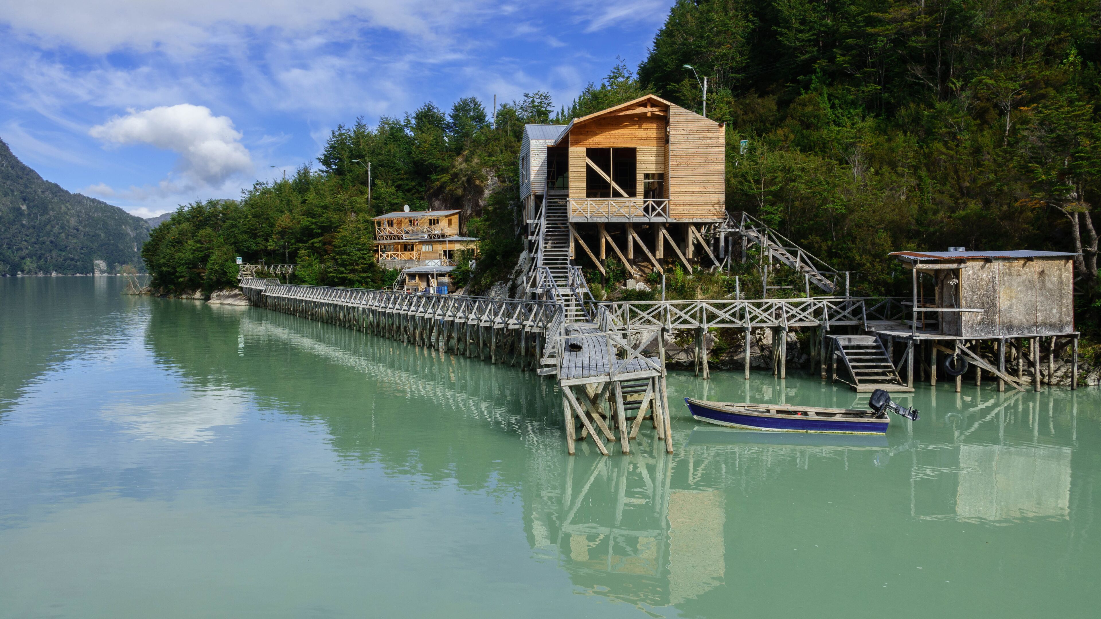 A wooden dock extending into a calm lake, surrounded by lush greenery and a mountain in the background.
