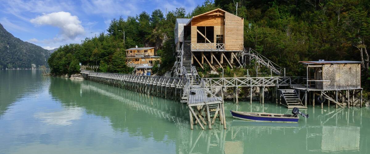 A wooden dock extending into a calm lake, surrounded by lush greenery and a mountain in the background.