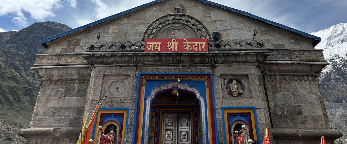 A stone temple with a blue roof and intricate carvings, surrounded by mountains.