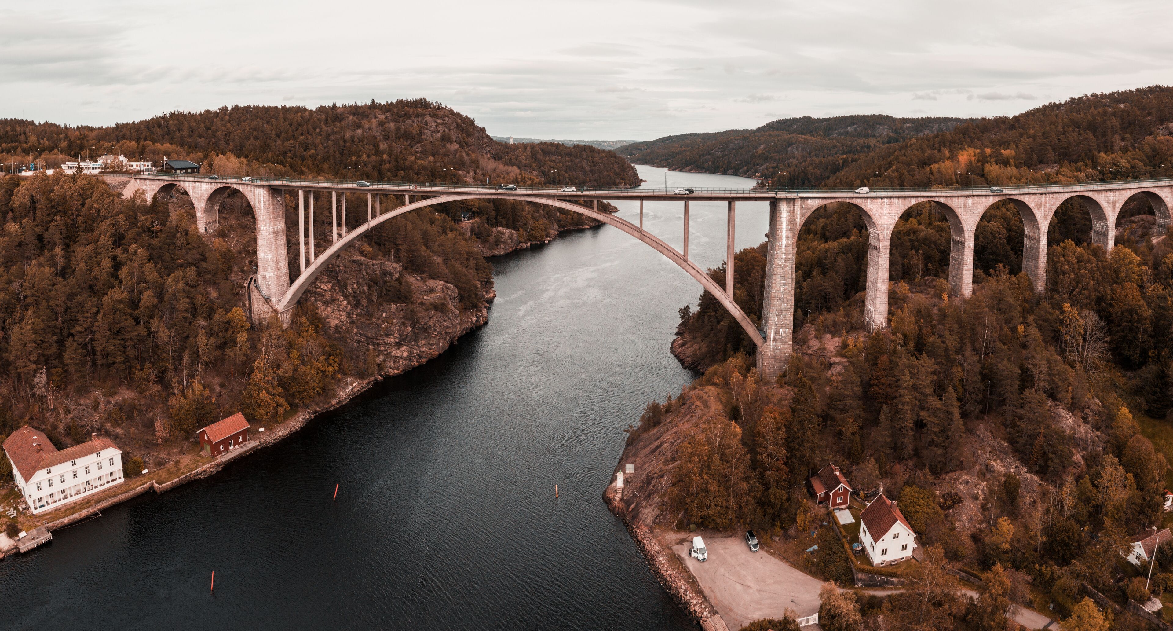 A large stone bridge spanning a river, surrounded by forested hills and a few buildings.
