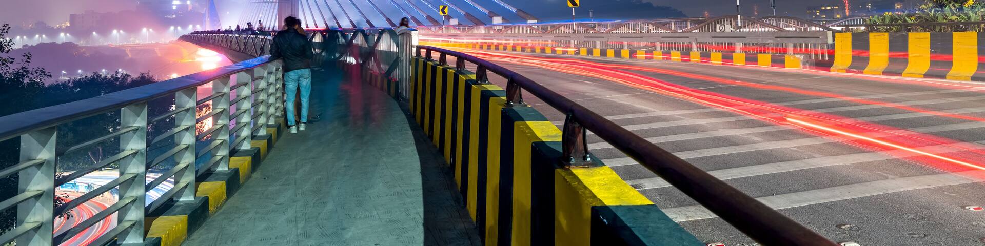 A lit bridge at night with a pedestrian walkway and traffic lights.