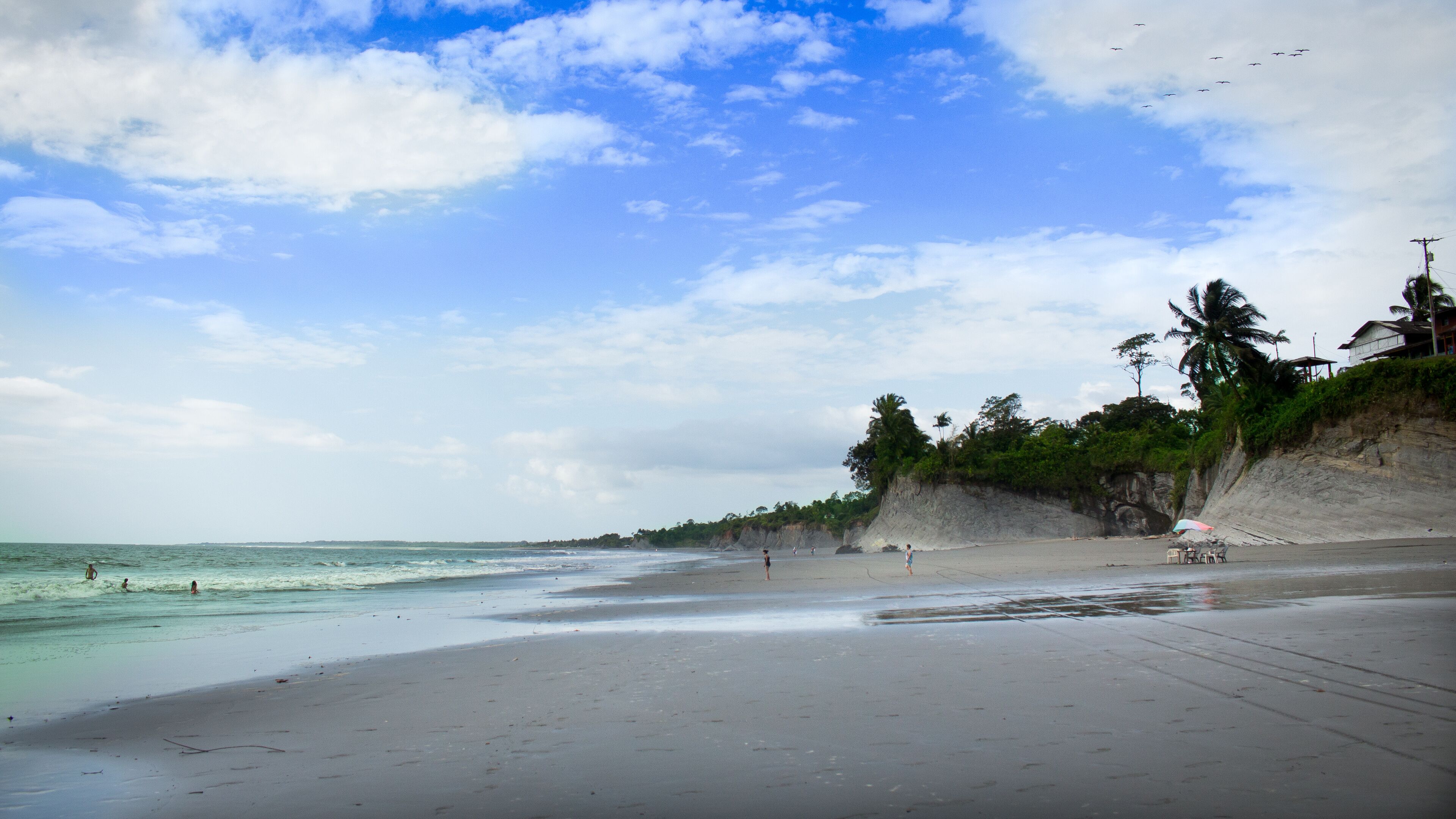 A beach with clear turquoise water, a sandy shore, and a cliff with vegetation.