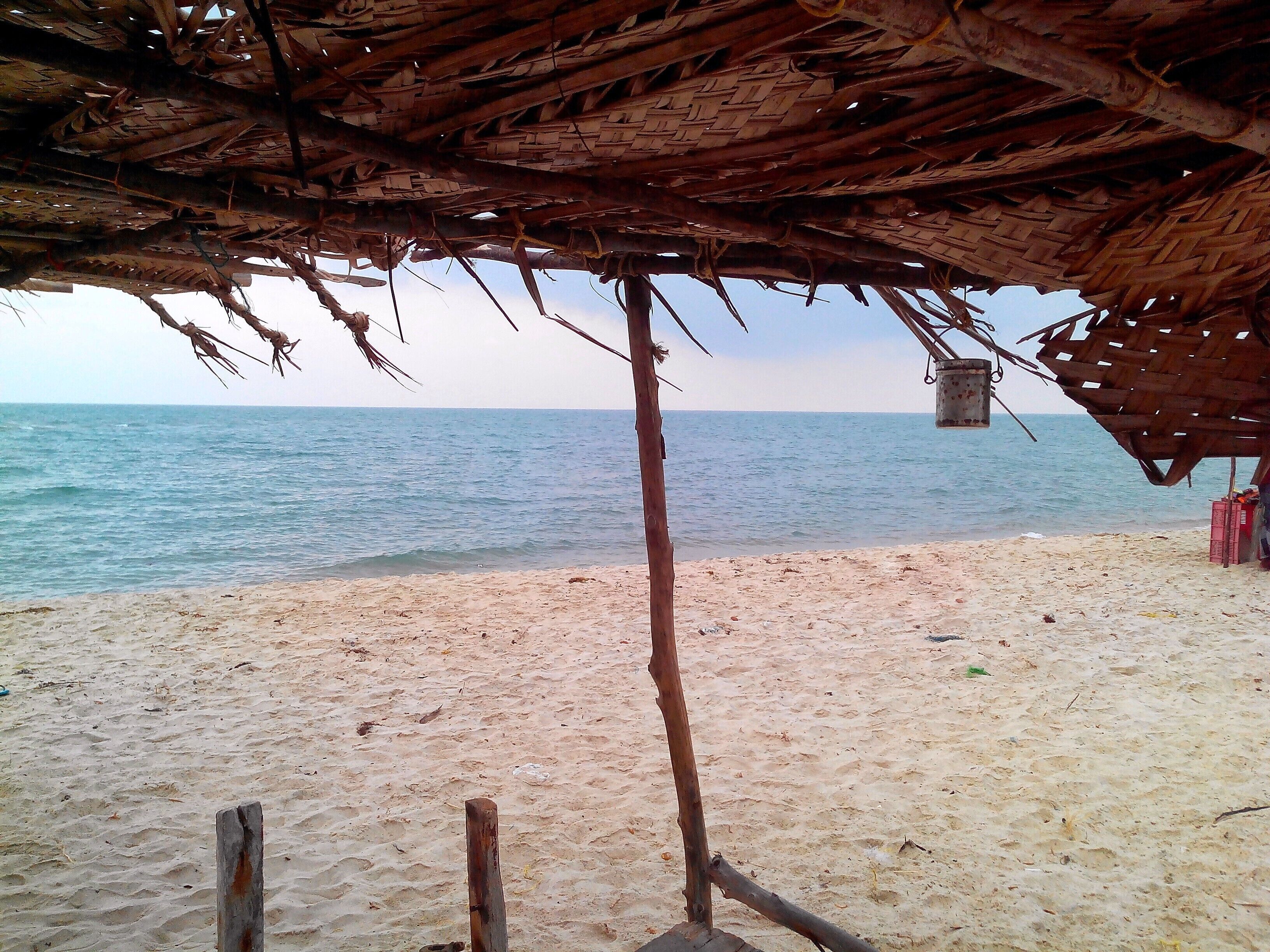A beach with a thatched roof structure, a wooden post, and a view of the calm sea.