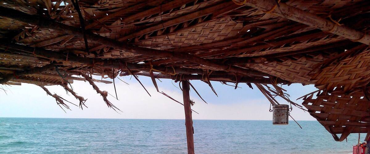 A beach with a thatched roof structure, a wooden post, and a view of the calm sea.