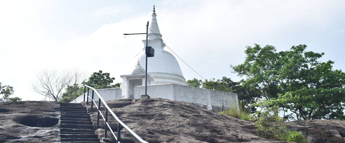 A white stupa on a rocky hill with a staircase leading up to it.