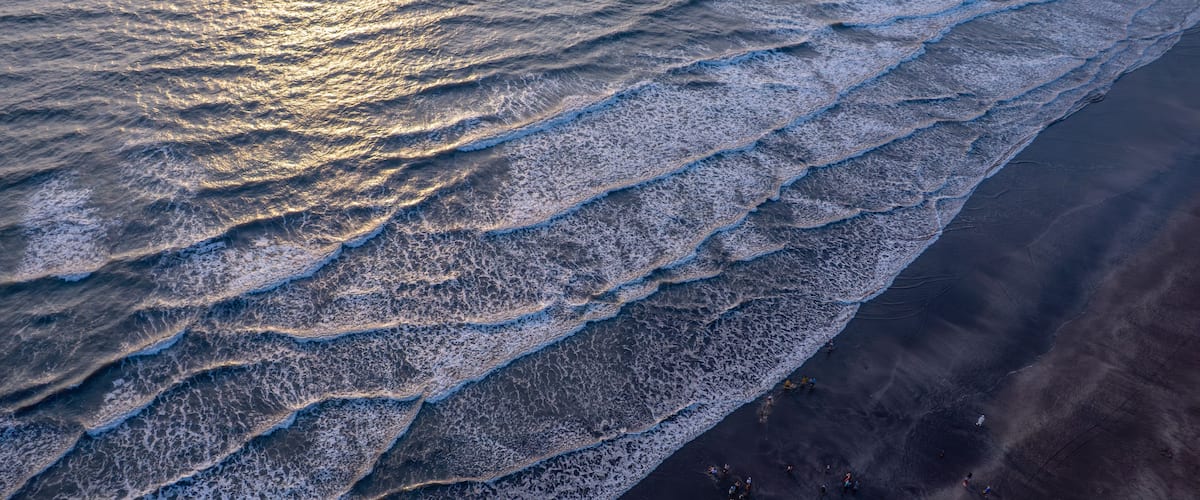 A beach with waves crashing onto the shore and people walking along the beach.