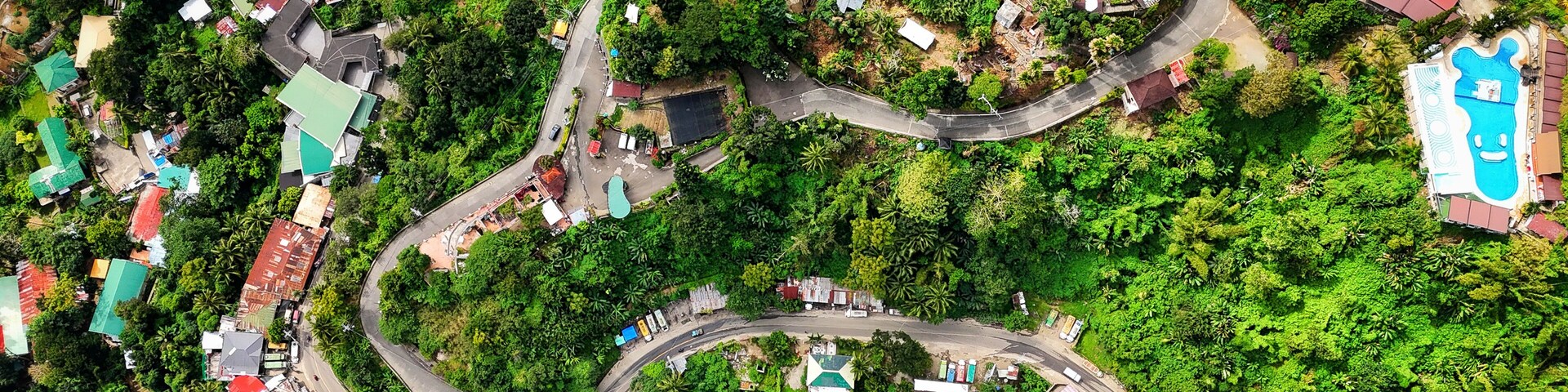 An aerial view of a winding road through a lush, green landscape with scattered buildings and houses.