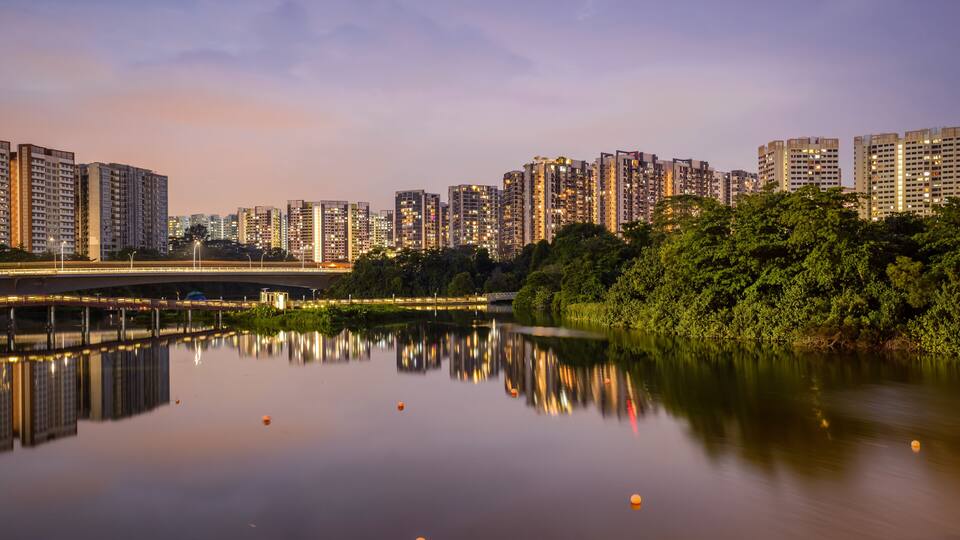A cityscape with high-rise buildings, a river reflecting lights, and a bridge.