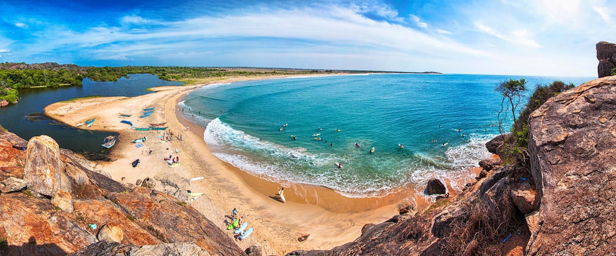 A coastal beach with clear turquoise waters, sandy shore, and rocky cliffs.