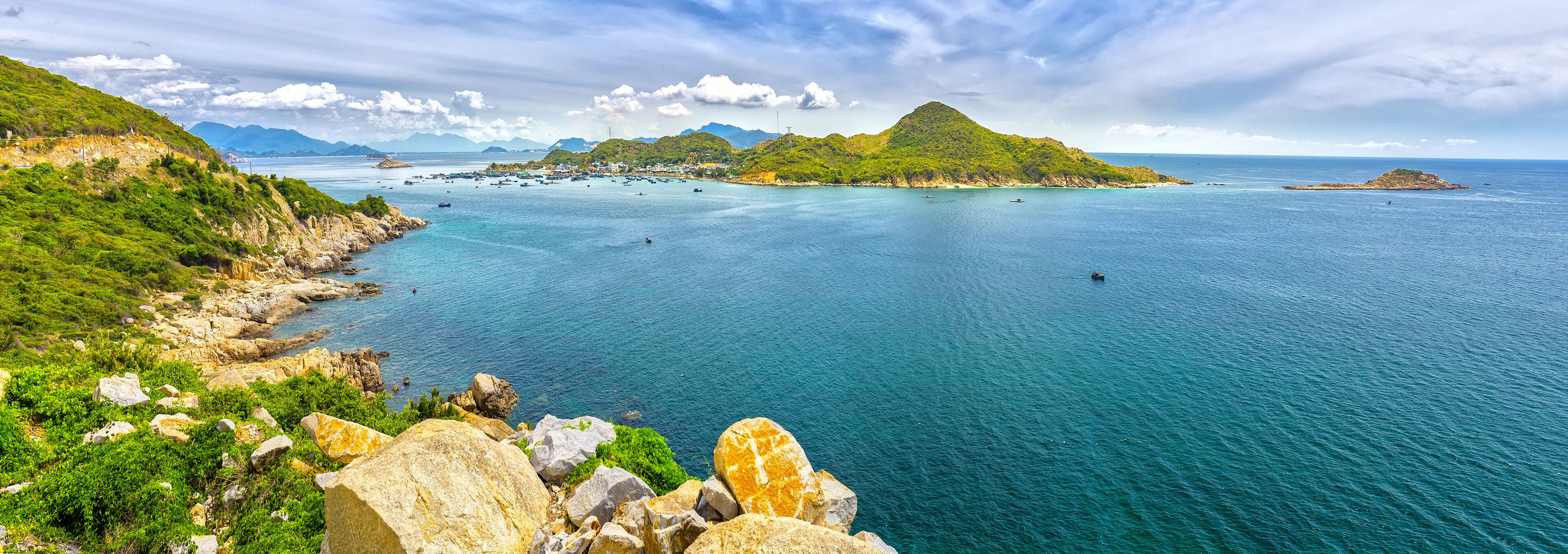 A coastal landscape with a prominent green hill, rocky shoreline, and calm sea.