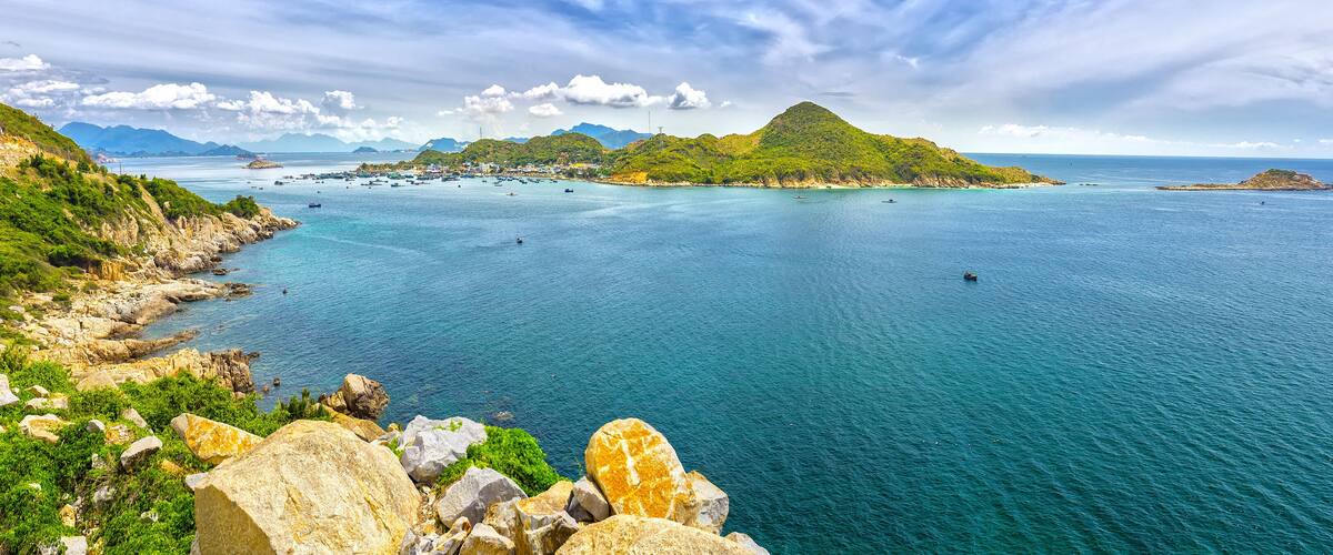 A coastal landscape with a prominent green hill, rocky shoreline, and calm sea.