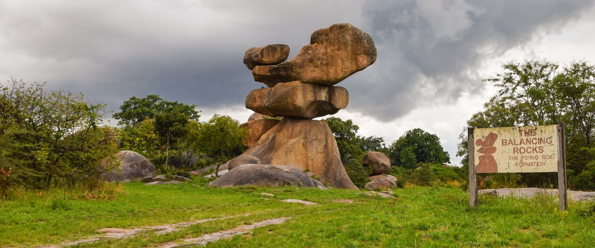 A large balancing rock formation with a sign in the foreground.