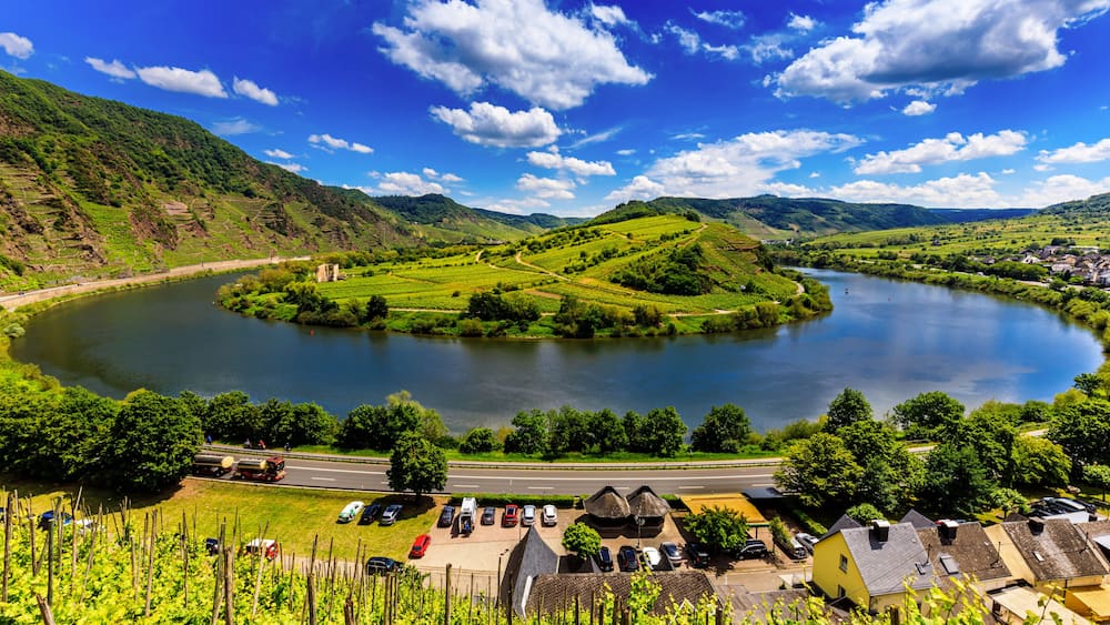 Un lac entouré de collines verdoyantes, une route et un petit village avec des maisons.