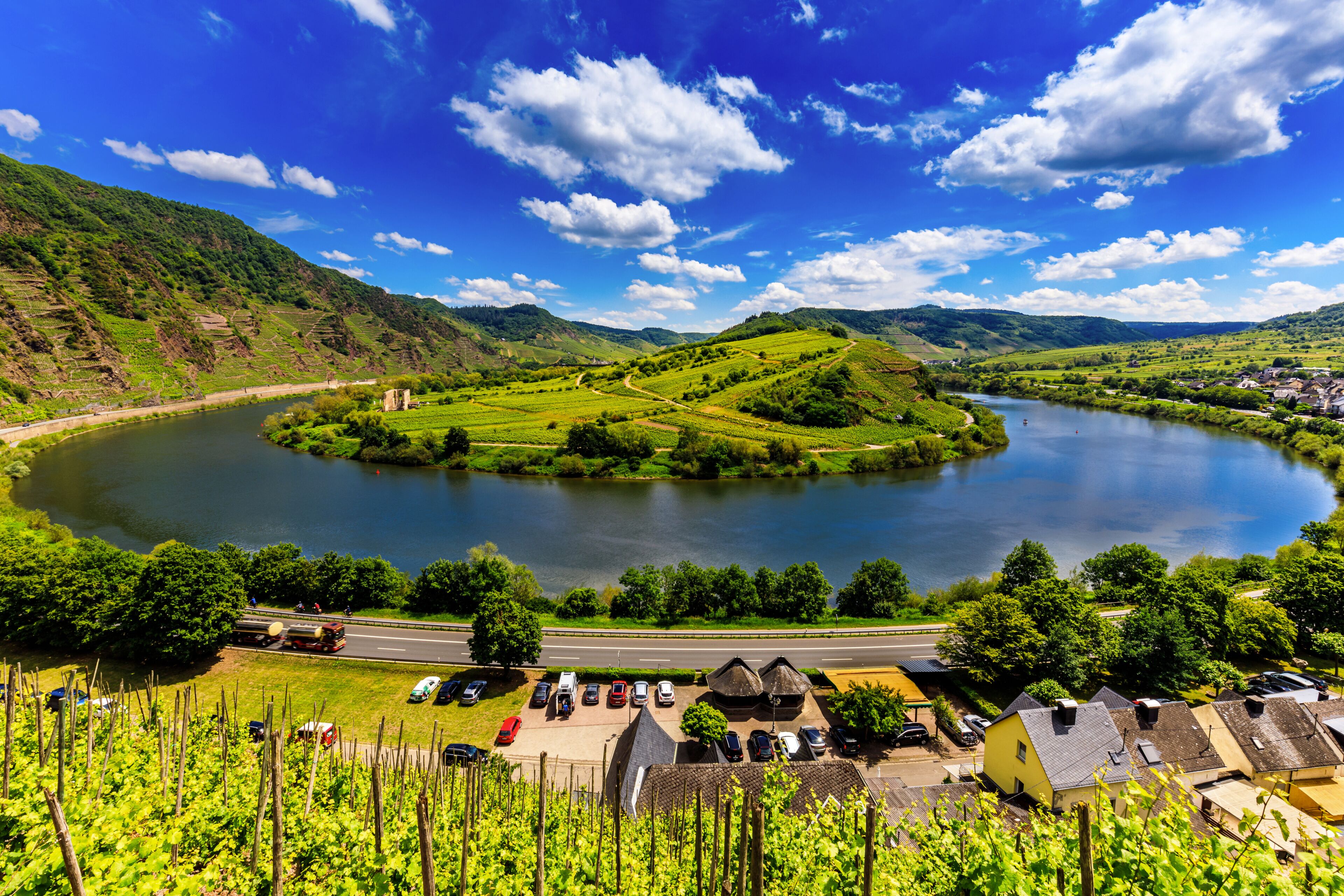 A lake surrounded by green hills, a road, and a small village with houses.
