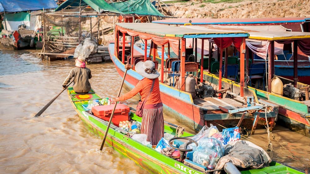 A colorful boat with a person rowing, surrounded by other boats and makeshift structures.