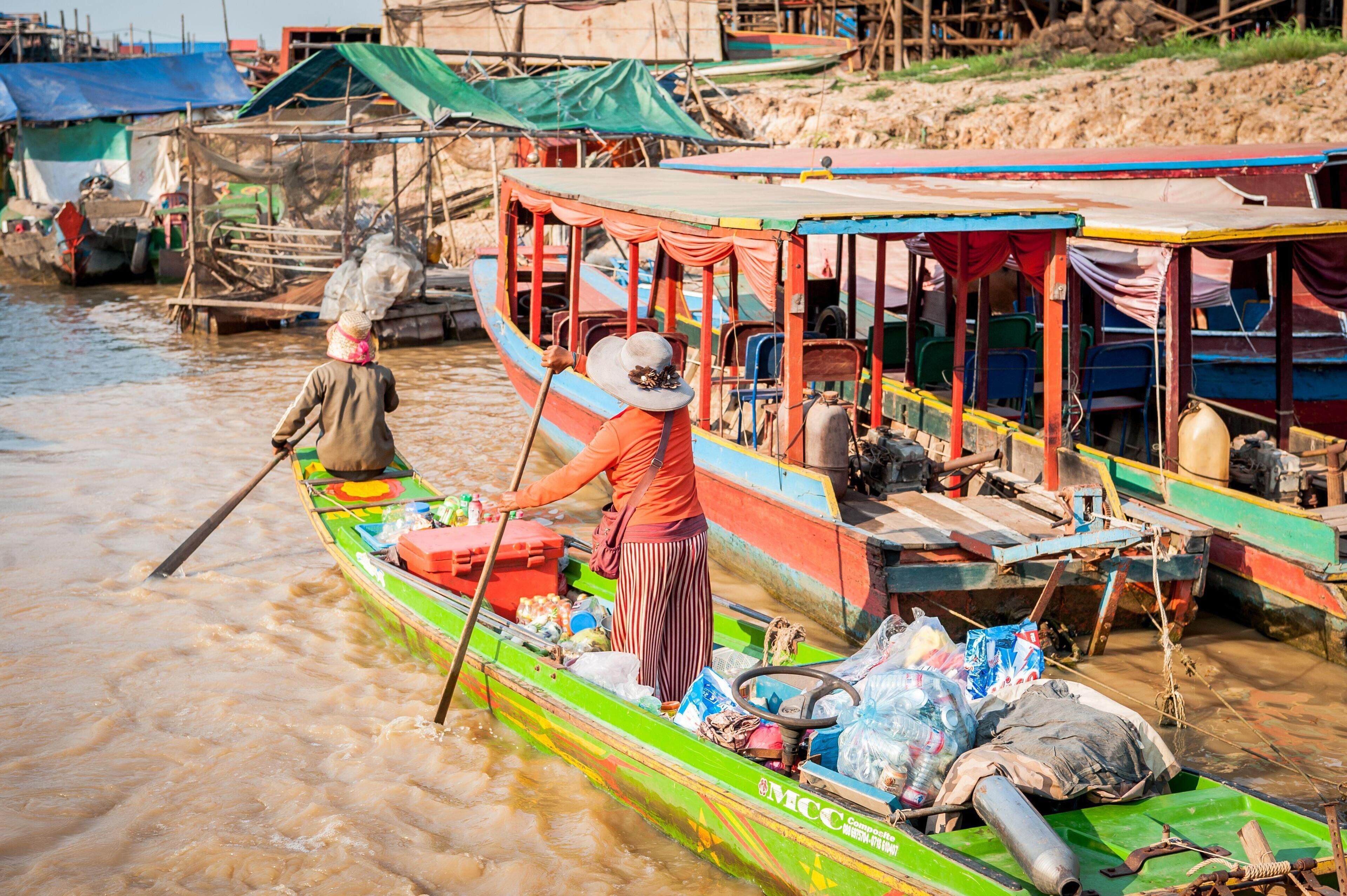 A colorful boat with a person rowing, surrounded by other boats and makeshift structures.