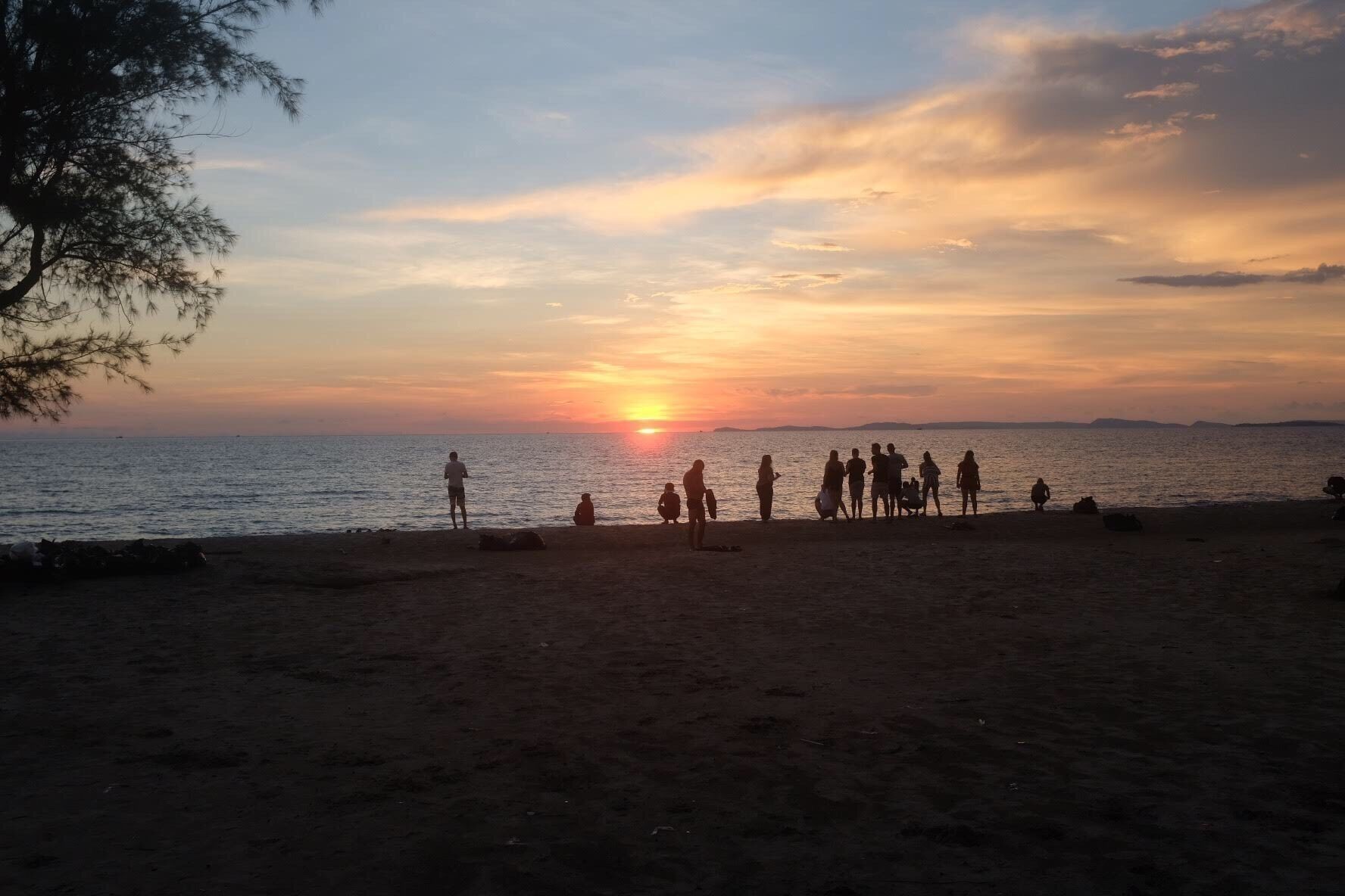 A beach at sunset with people gathered on the sand.
