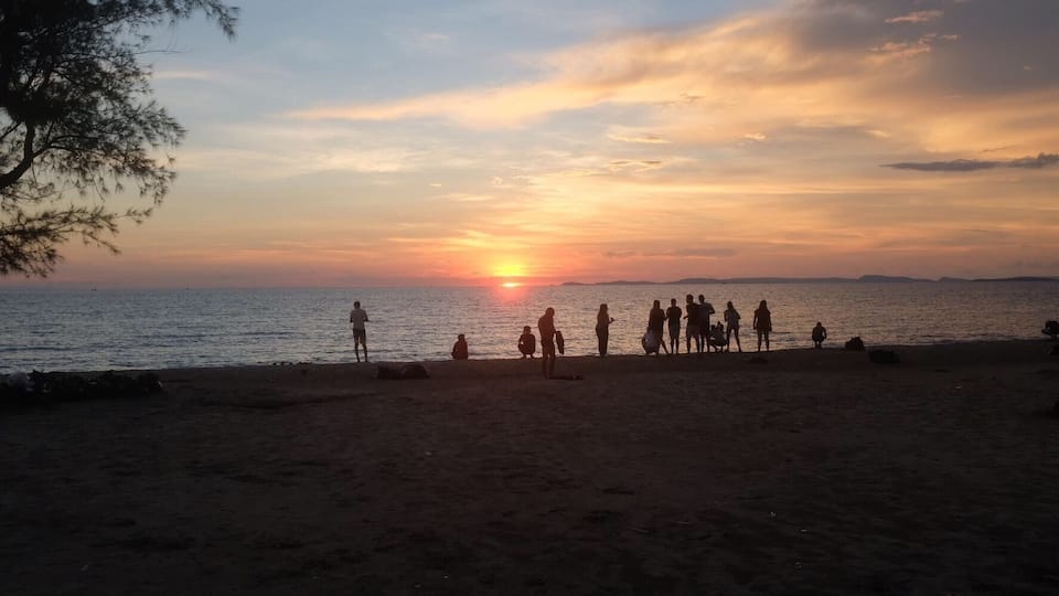 Una playa al atardecer con gente reunida en la arena.