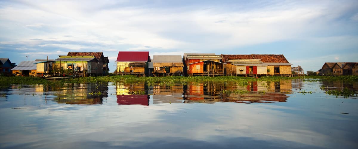 A cluster of traditional houses with red roofs on stilts over a body of water.
