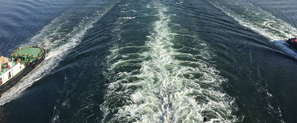 A river with two large bridges and a boat creating waves.