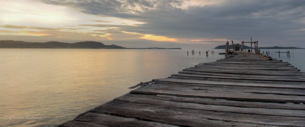 A wooden pier extending into calm water with a sunset sky.