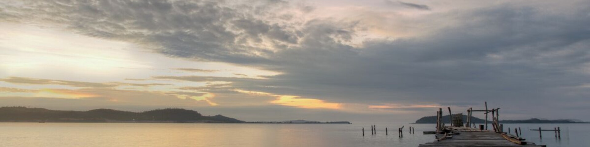 A wooden pier extending into calm water with a sunset sky.