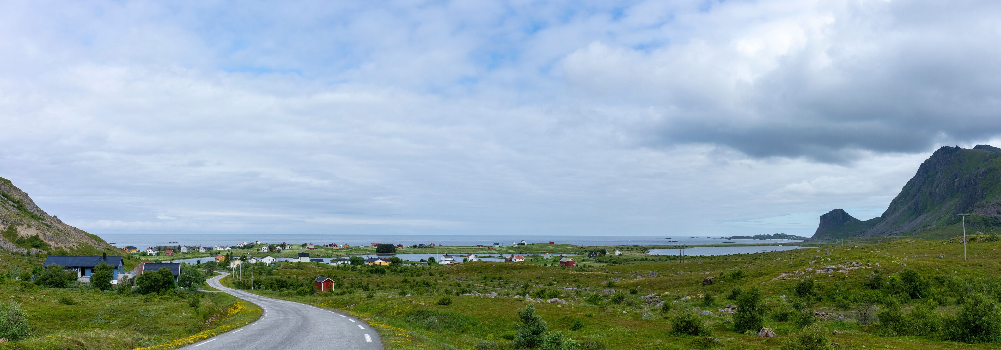 A coastal road winding through a rural landscape with houses, a body of water, and a mountain in the distance.