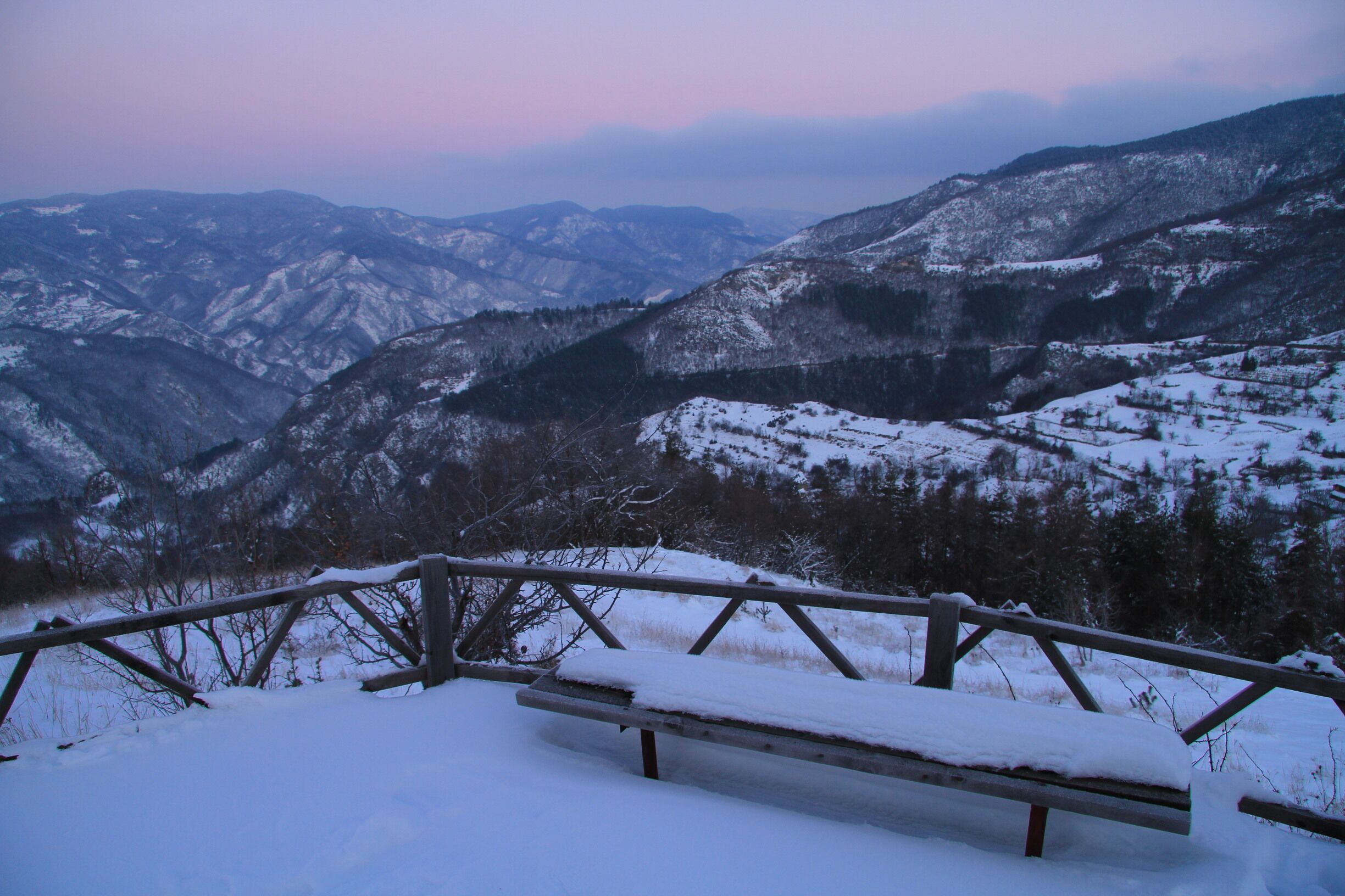 A snow-covered bench overlooking a mountainous landscape.