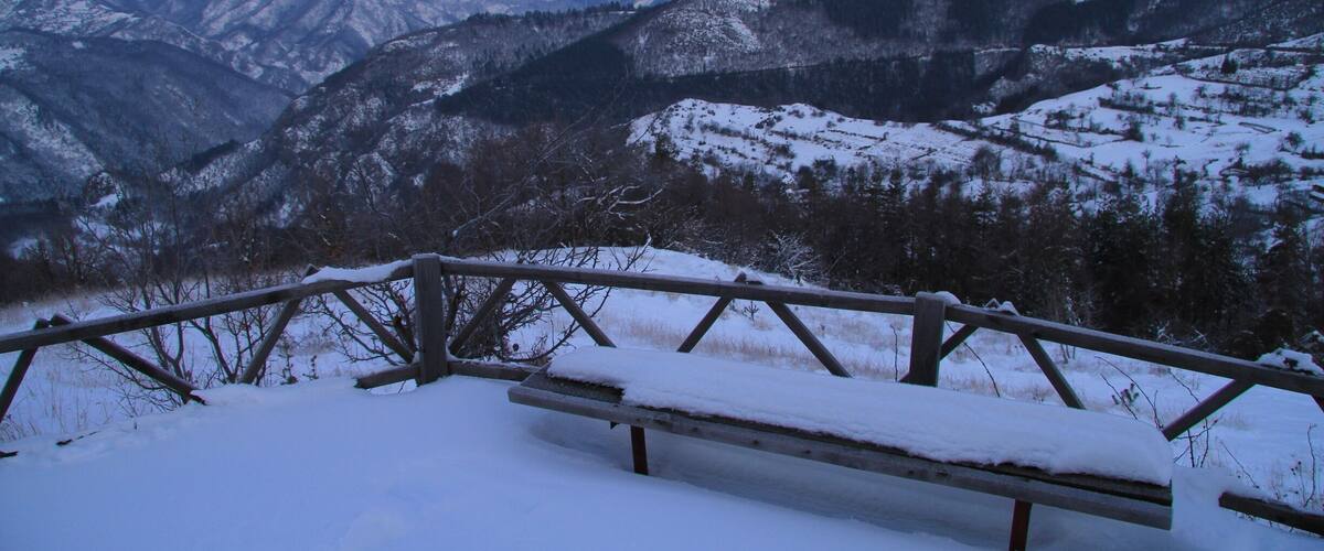 A snow-covered bench overlooking a mountainous landscape.