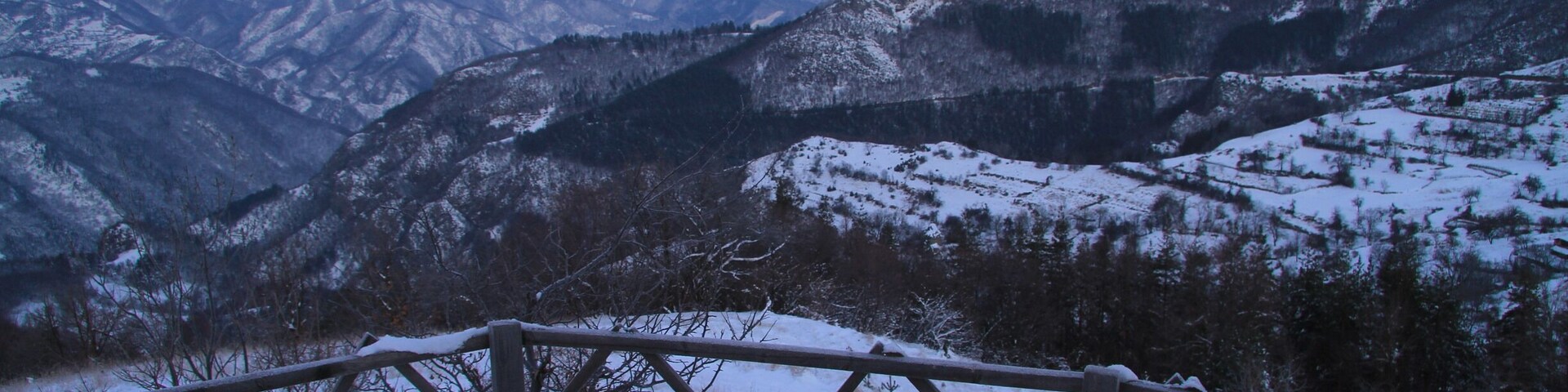 A snow-covered bench overlooking a mountainous landscape.