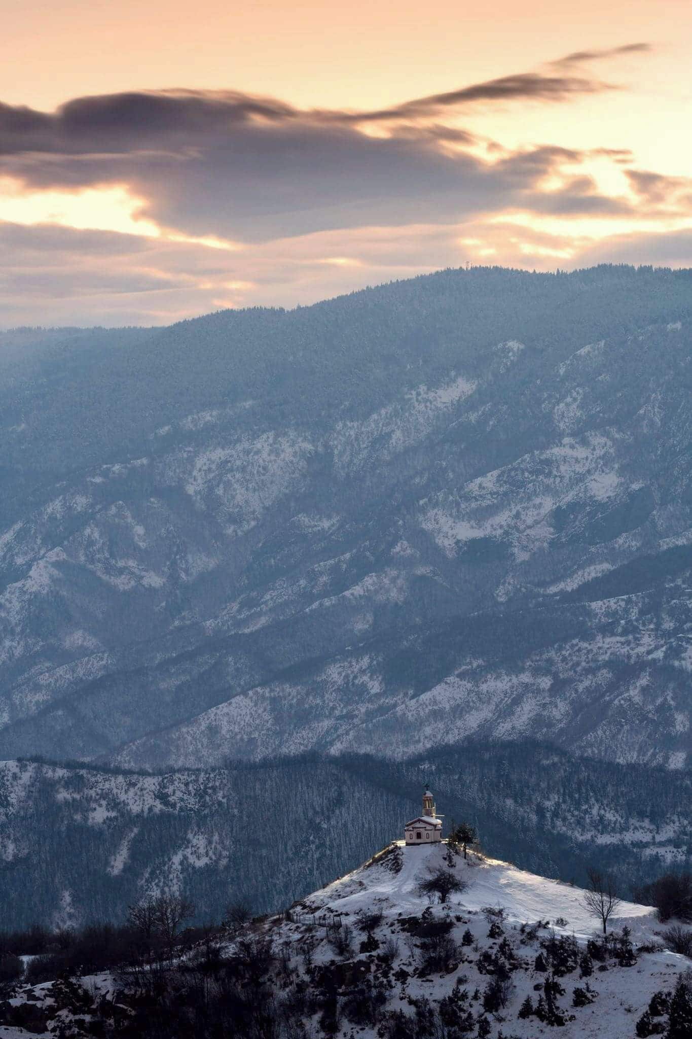 A snow-covered mountain with a small church on a hill.