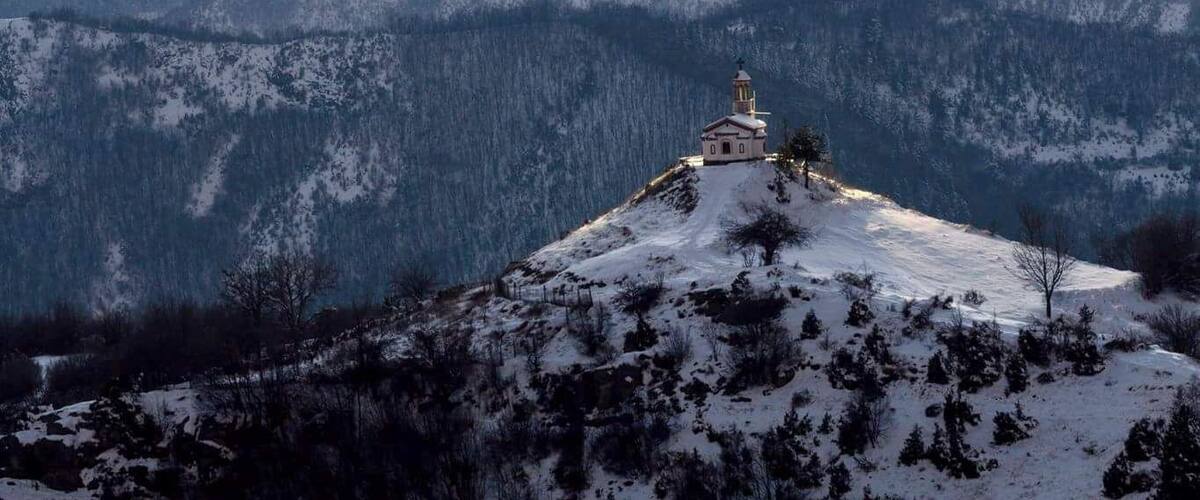 A snow-covered mountain with a small church on a hill.