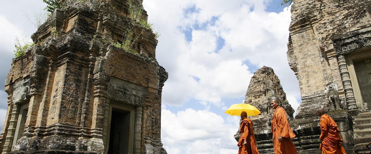 Ancient stone structures with carvings and a monk holding an umbrella.