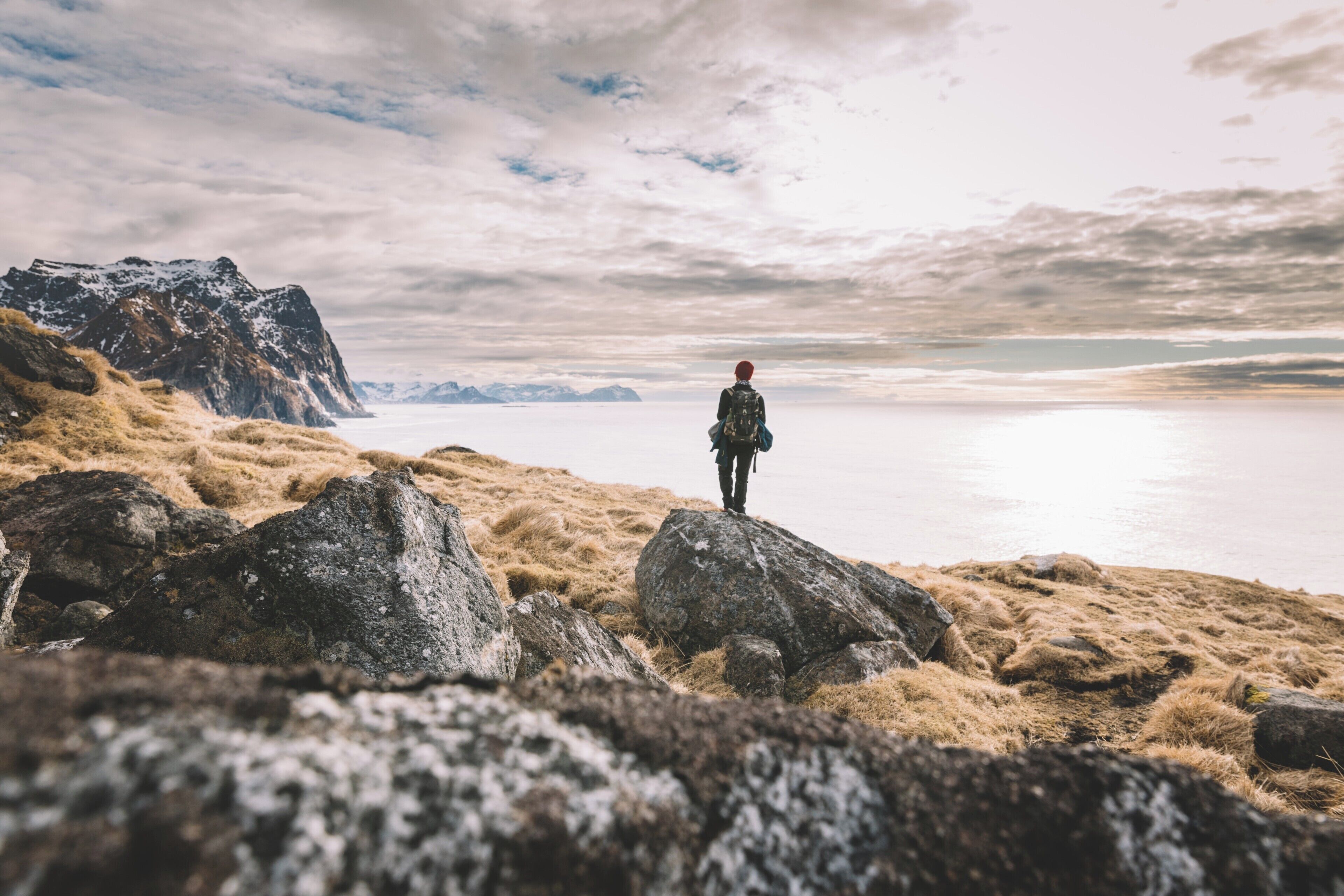 A person standing on a rocky outcrop overlooking a calm body of water with mountains in the distance.