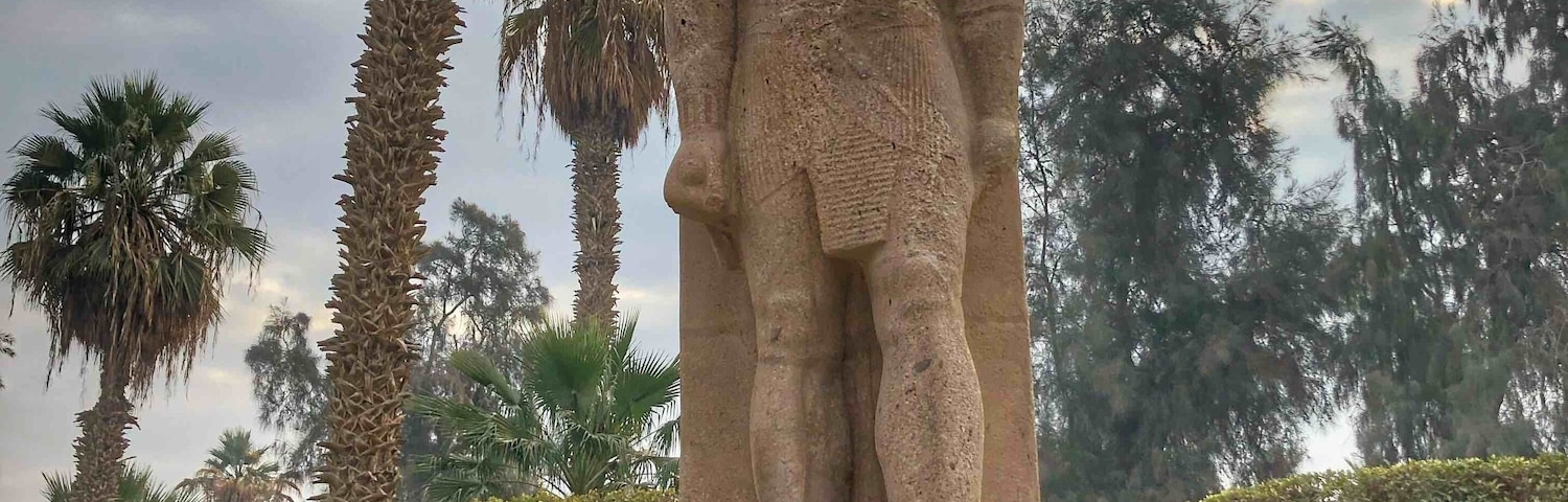 A stone statue of a figure in a park with palm trees and benches.
