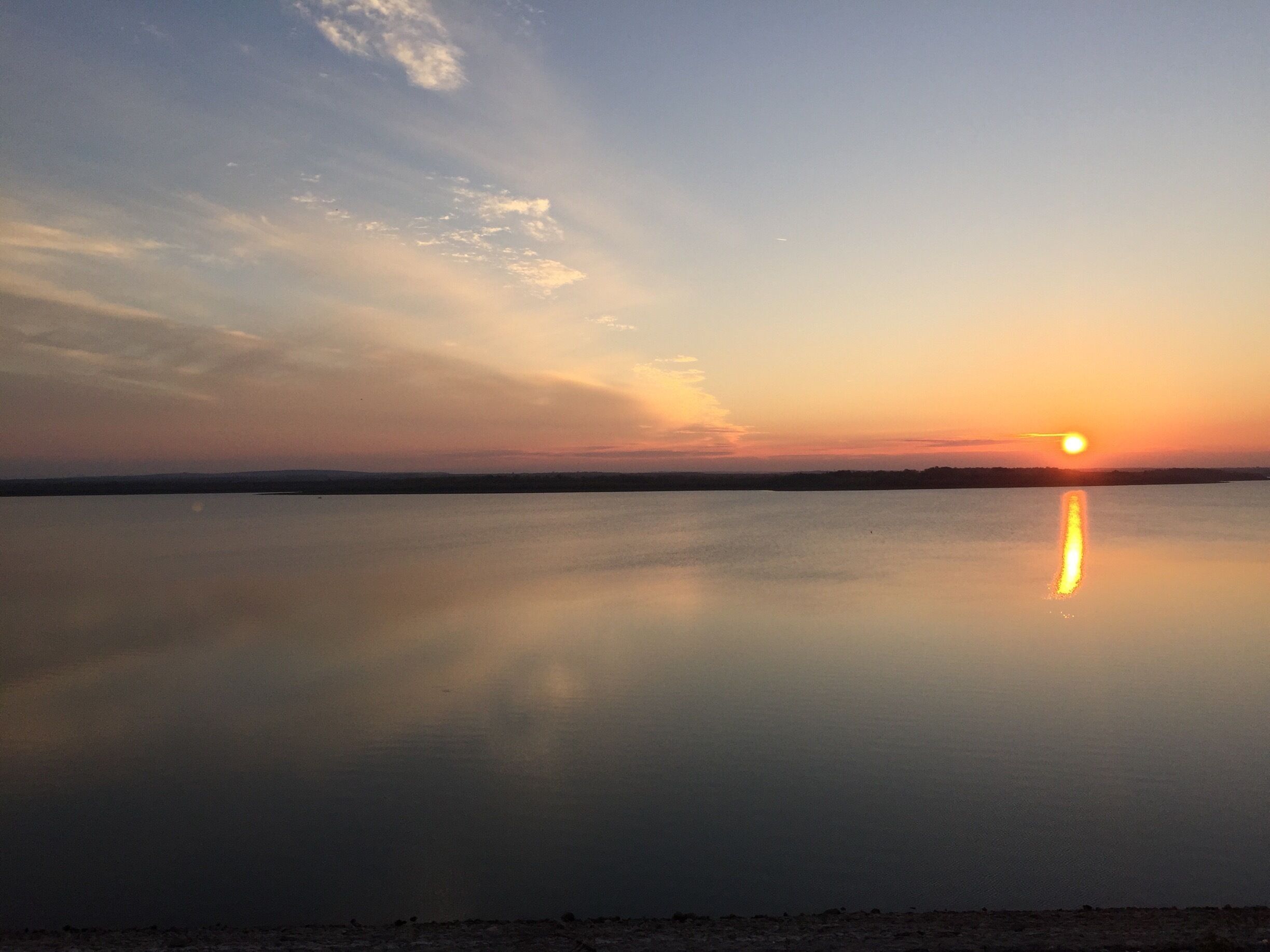 A sunset over a calm lake with a clear reflection of the sun and sky.