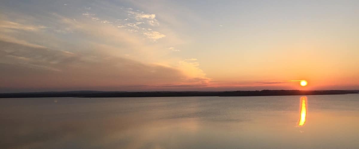 A sunset over a calm lake with a clear reflection of the sun and sky.