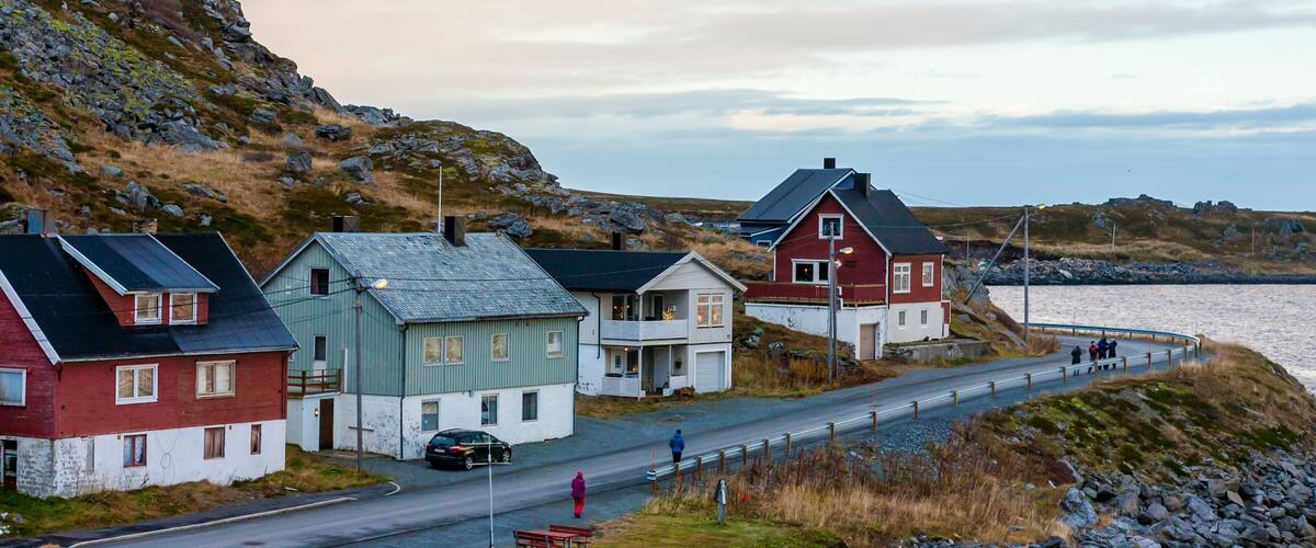 A coastal village with houses by the sea, a road, and rocky hills.