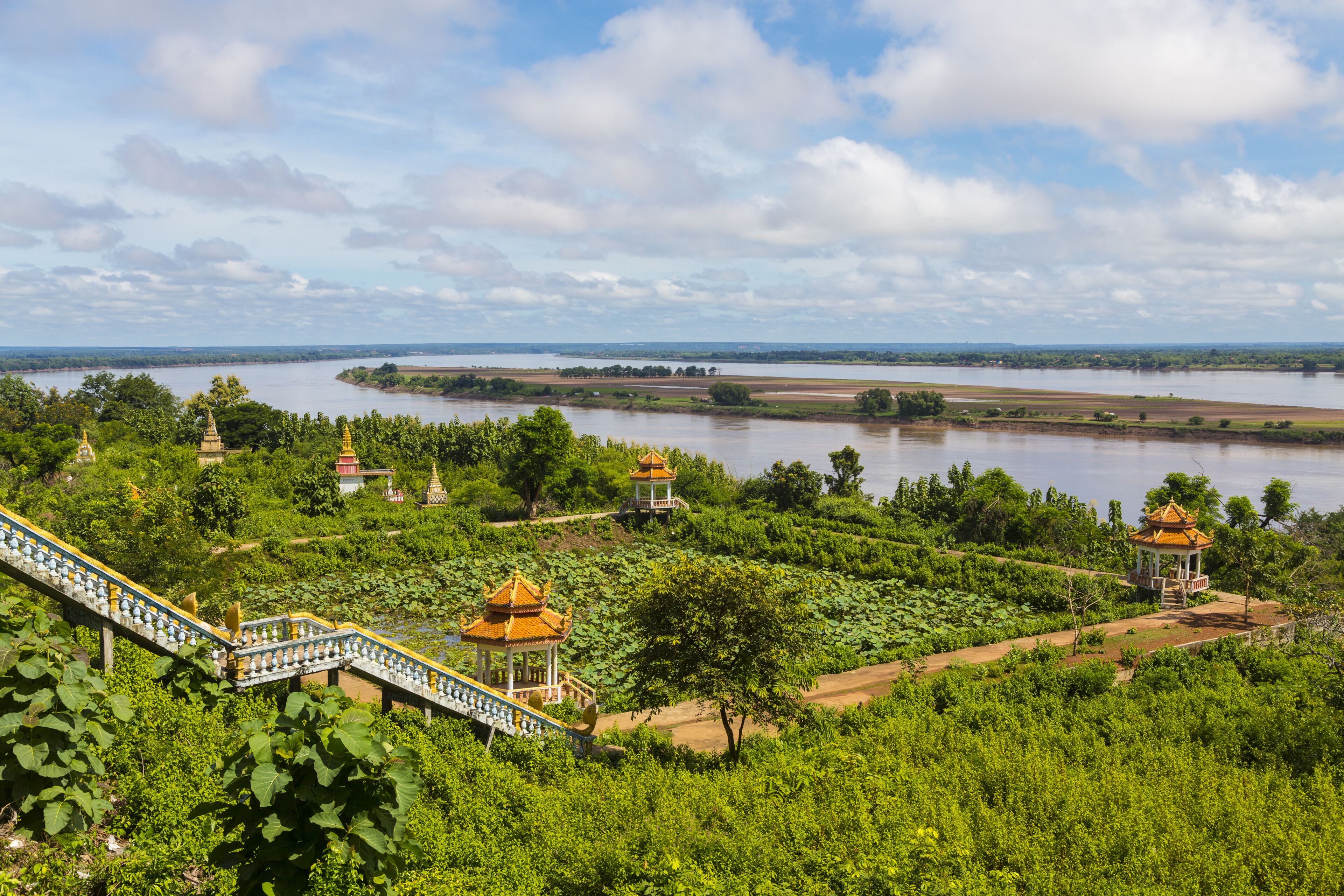 A lush green landscape with a river, lotus ponds, and traditional yellow-roofed pavilions.