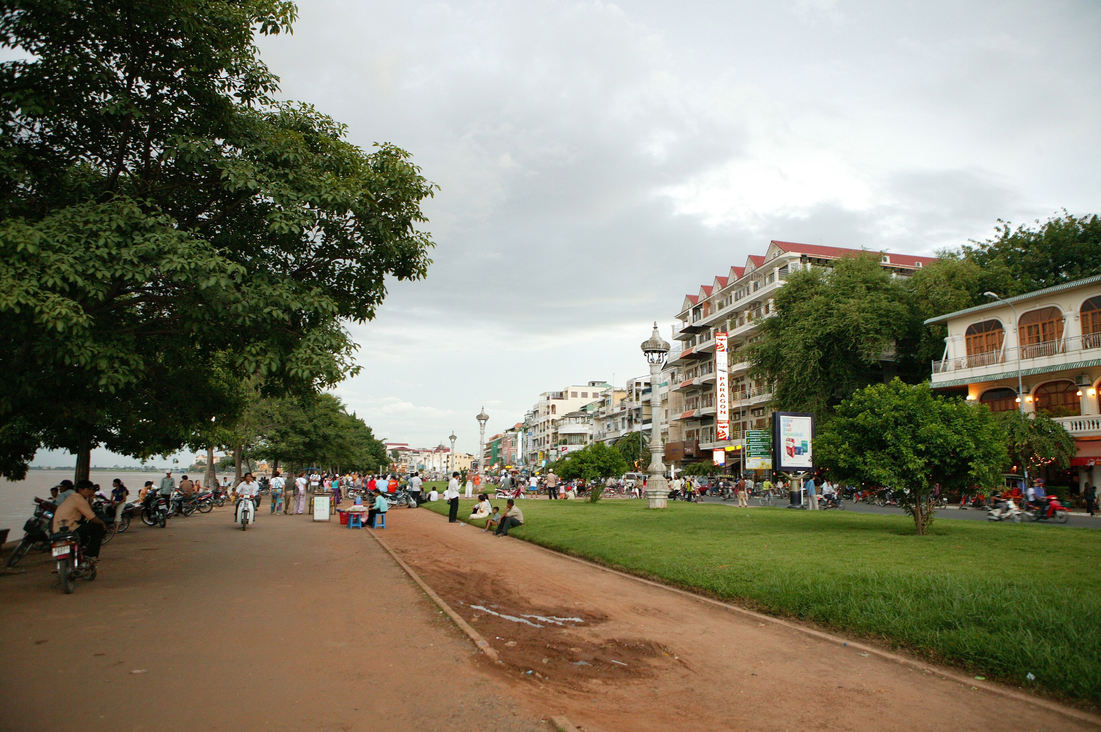 A riverside promenade with people walking, sitting, and parked motorcycles.