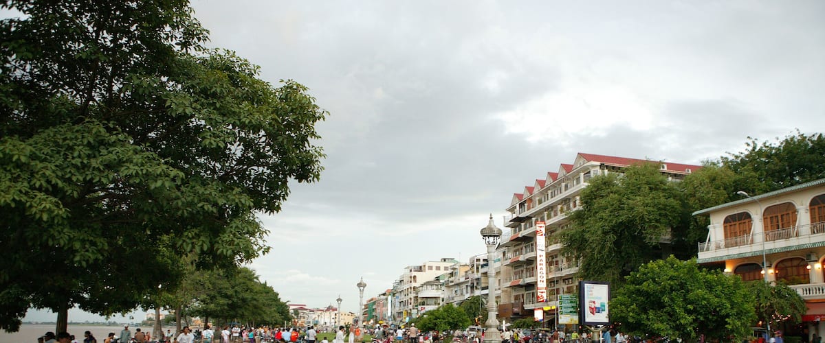 A riverside promenade with people walking, sitting, and parked motorcycles.