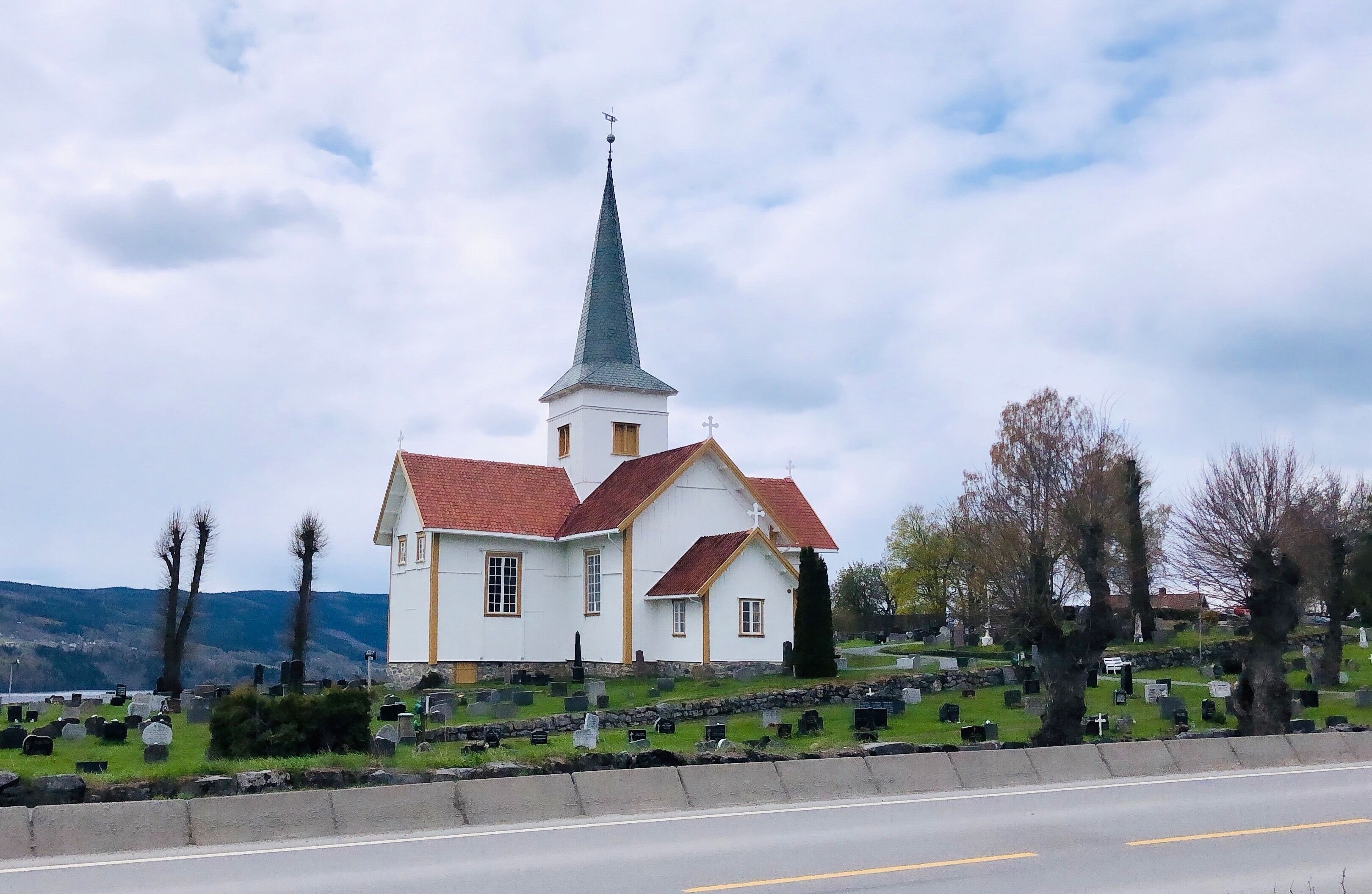 A white church with a red roof and a tall steeple, surrounded by a cemetery with gravestones.