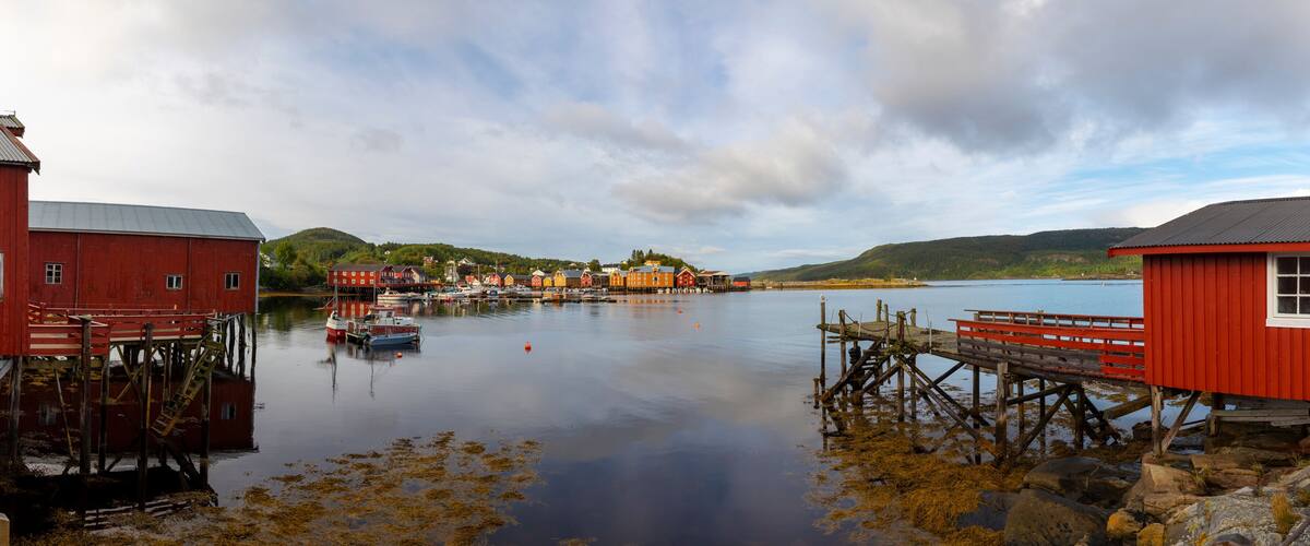 A coastal village with red buildings, wooden docks, and calm water.