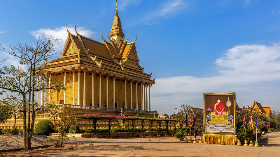 A traditional Thai temple with a golden spire, a large Buddha statue, and a well-maintained garden.